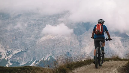 Mountainbiker fährt auf Bergweg mit nebligen Bergen im Hintergrund