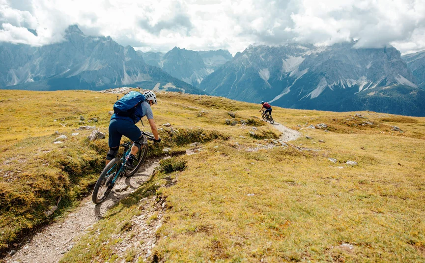 Mountainbike-Urlaub in der Region 3 Zinnen Dolomites © David Karg Zwei Mountainbiker fahren auf einem Bergpfad mit Alpen im Hintergrund