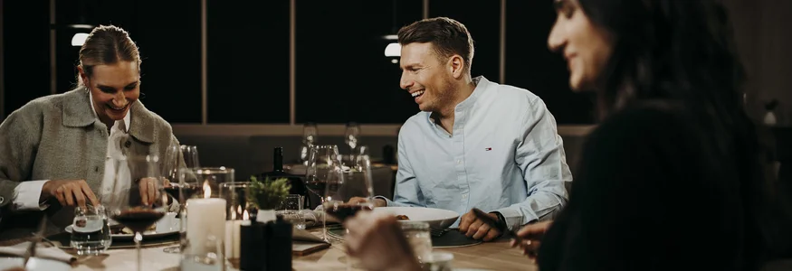 Bye bye Tauernhof, hello Dips&Drops! Drei Menschen lachen gemeinsam bei einem Abendessen am Tisch