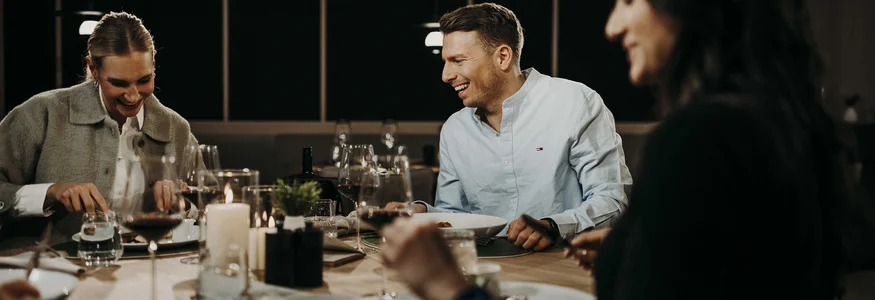 Drei Menschen lachen gemeinsam bei einem Abendessen am Tisch
