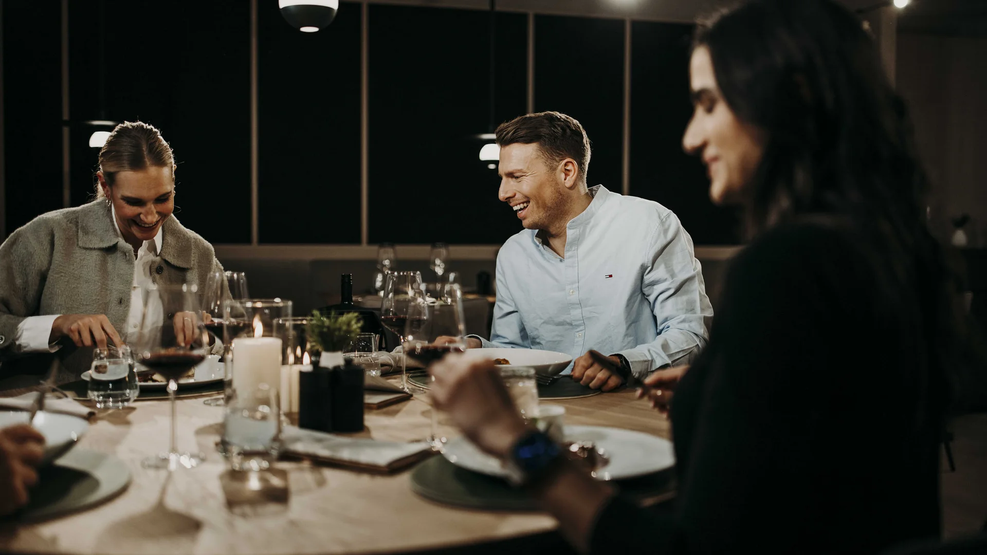 Drei Menschen lachen gemeinsam bei einem Abendessen am Tisch