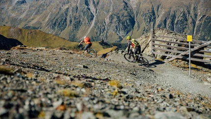Zwei Mountainbiker fahren auf einem gebirgigen Schotterweg mit Bergen im Hintergrund