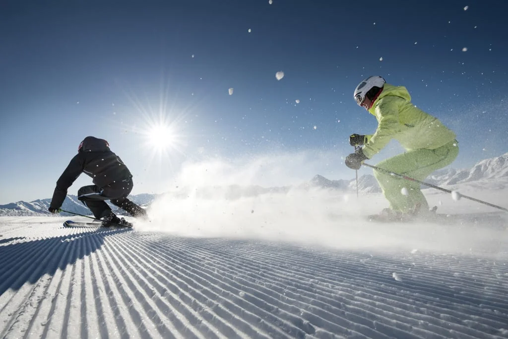 Twee skiërs skiën op een zonnige besneeuwde helling
