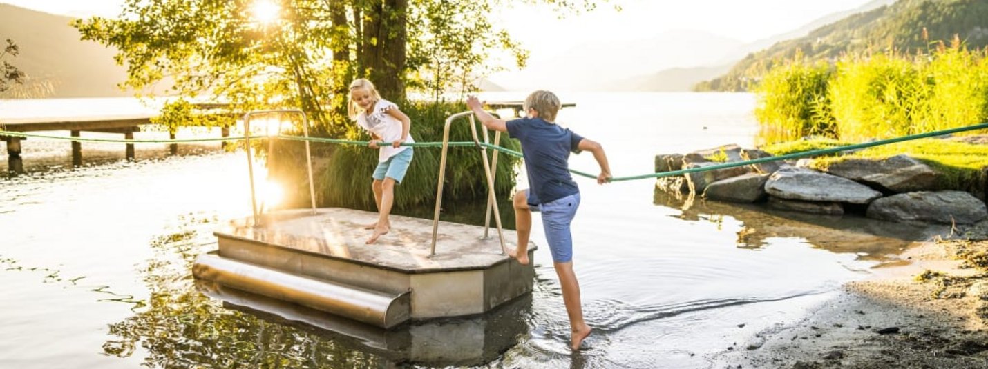 Familienhit im Früh-& Spätsommer 7 Nächte Kinder spielen an einem See auf einer kleinen Fähre bei Sonnenuntergang