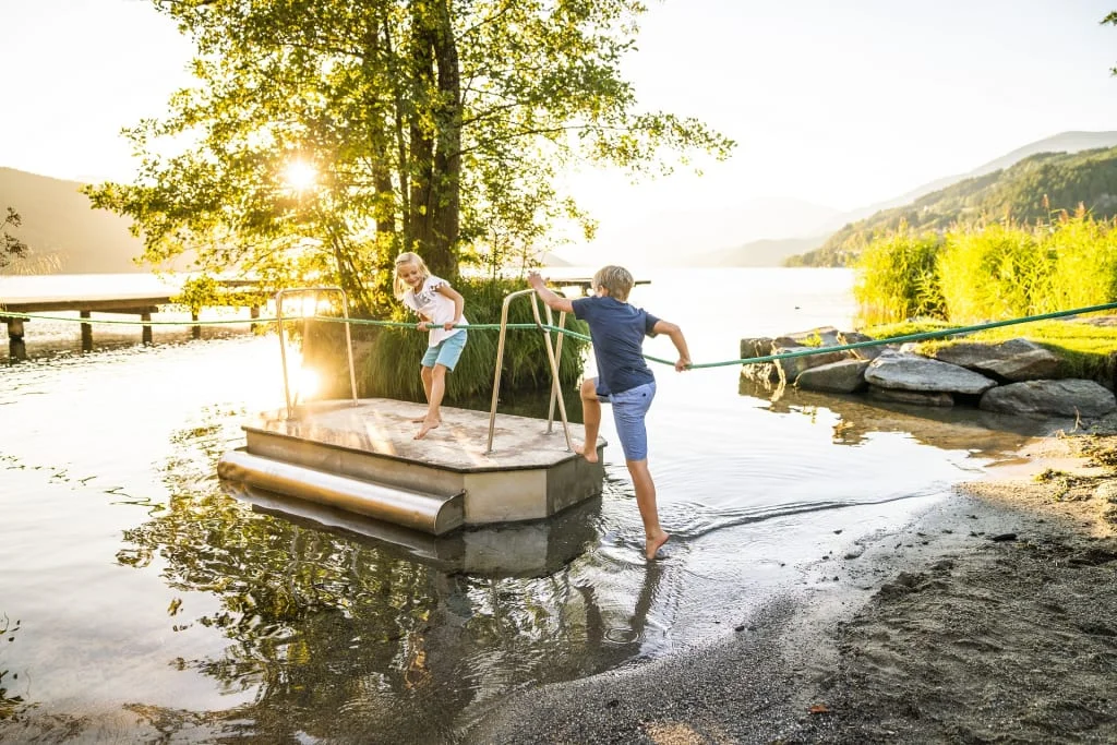 Kinder spielen an einem See auf einer kleinen Fähre bei Sonnenuntergang