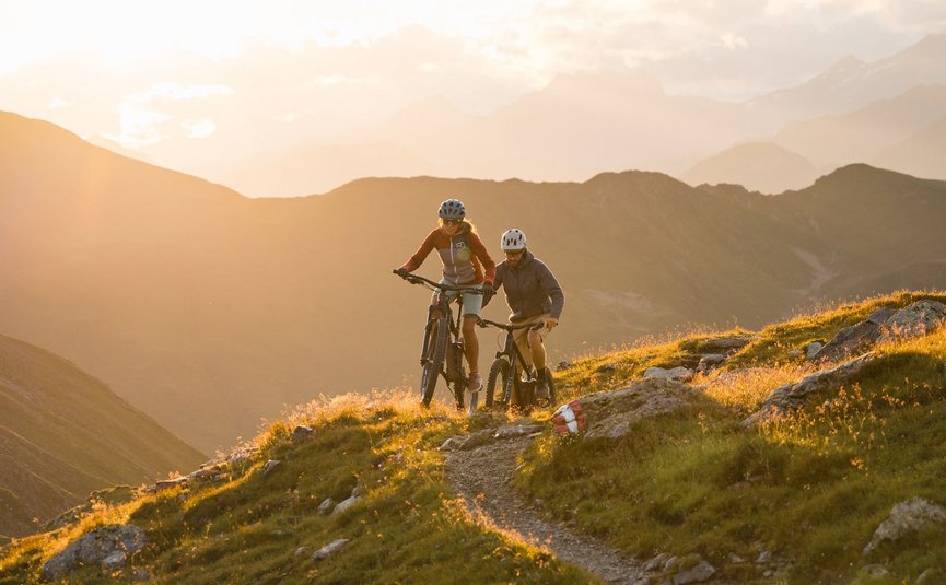 Zwei Mountainbiker fahren auf einem Bergweg bei Sonnenuntergang
