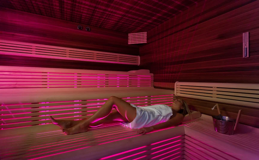Woman relaxing in sauna with purple lighting and white towel