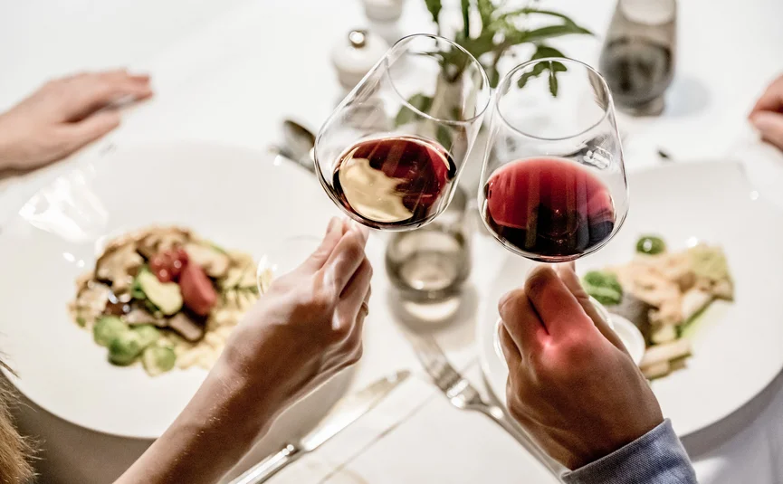 Zwei Personen stoßen mit Rotweingläsern über einem gedeckten Tisch an