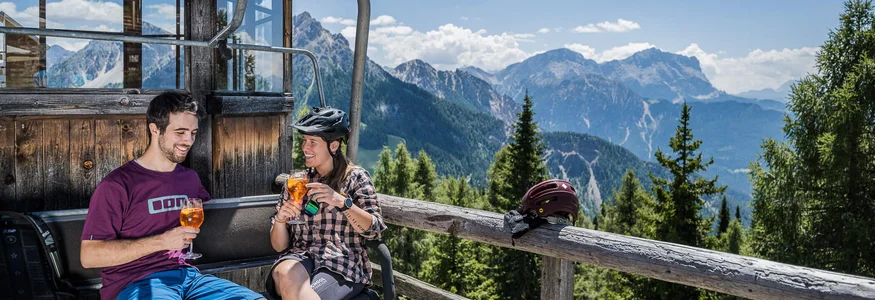 Zwei Mountainbiker trinken Getränke auf einer Berghütte mit Bergblick