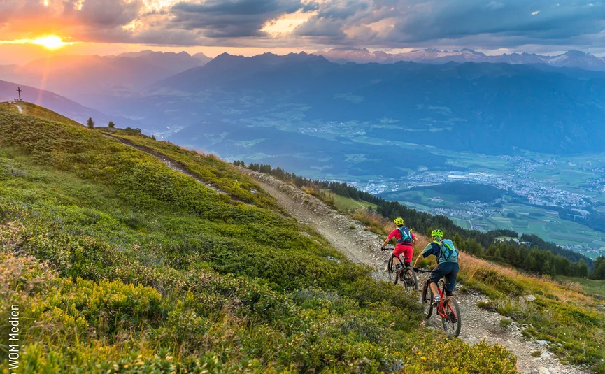 Zwei Mountainbiker fahren bei Sonnenuntergang auf einem Bergweg