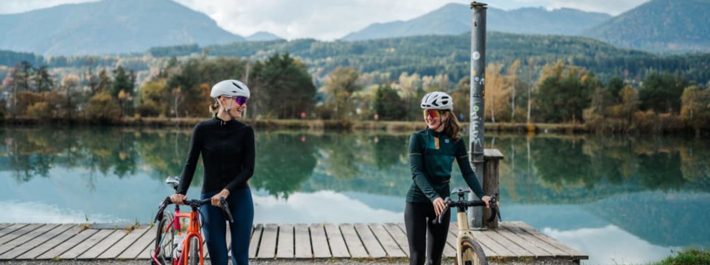 Gravel & Glory Twee vrouwelijke fietsers met fietsen bij het meer met bergen op de achtergrond