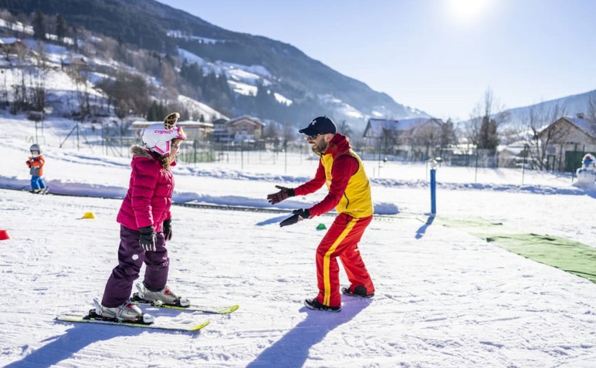 Ski instructor teaching child on snowy slope on a sunny day