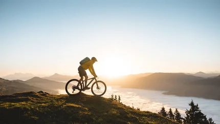 Mountainbiker bei Sonnenaufgang auf einem Hügel mit Nebel im Tal