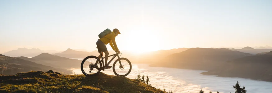 Mountainbiker bei Sonnenaufgang auf einem Hügel mit Nebel im Tal