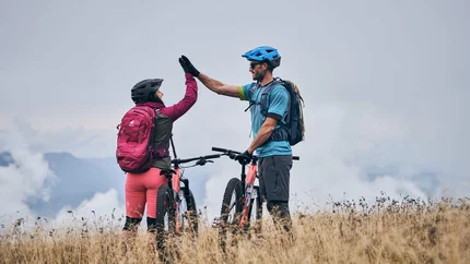 Zwei Mountainbiker geben sich auf einer Wiese einen High Five