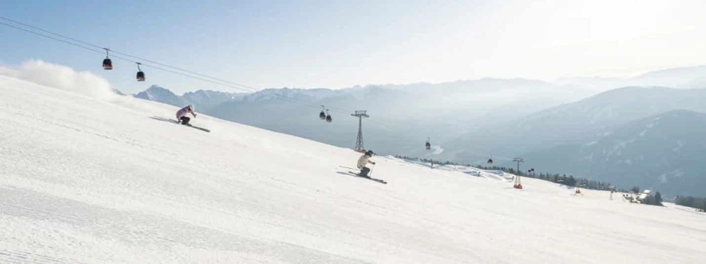 Skiers on a snowy slope with a cable car and mountains in the background