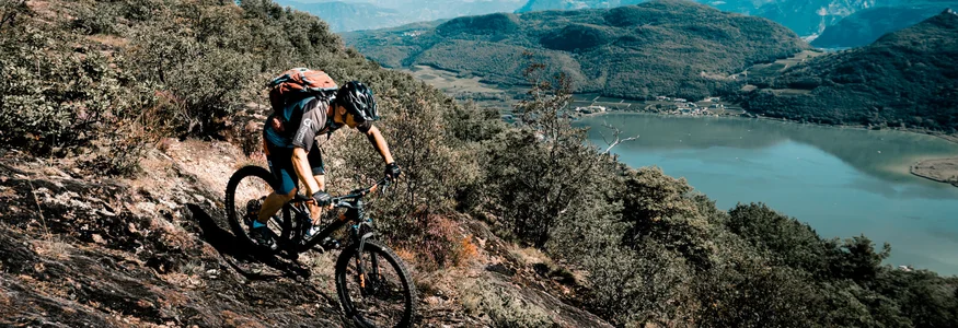 Mountainbiker fährt einen steilen Pfad mit Berg- und Seeblick