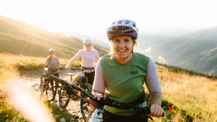 Drei Frauen mit Helmen beim Mountainbiken auf sonnigem Bergweg
