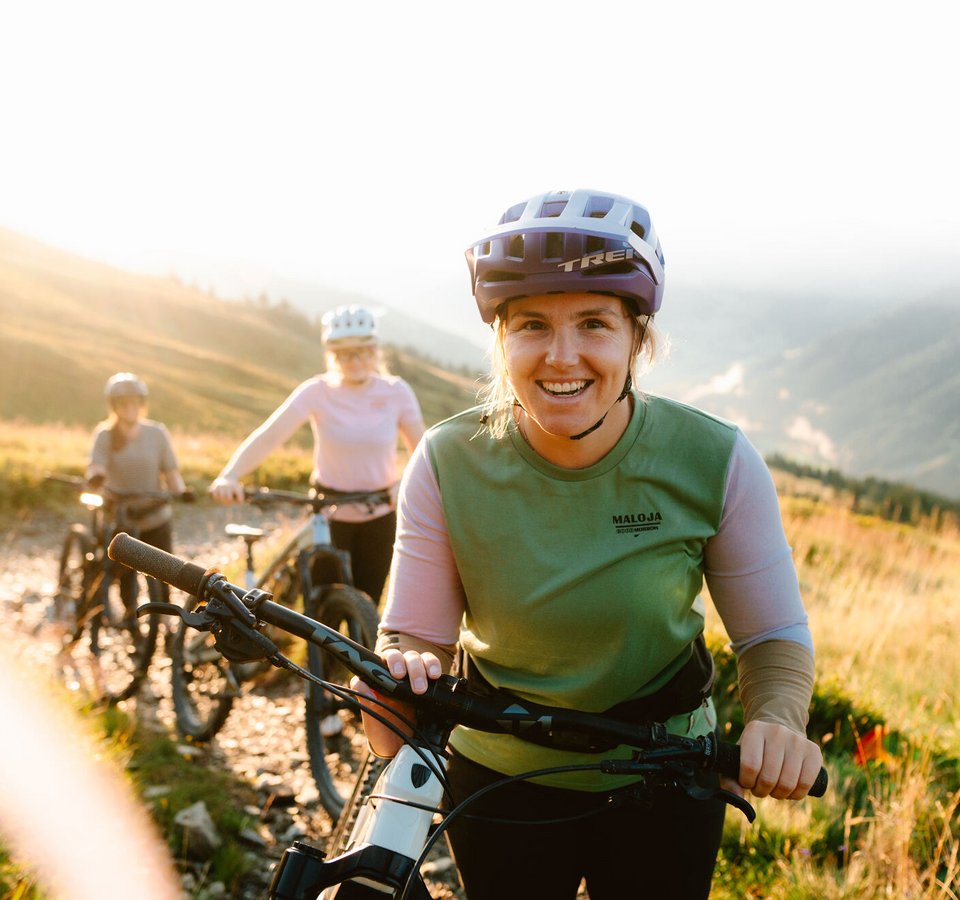 Drei Frauen mit Helmen beim Mountainbiken auf sonnigem Bergweg