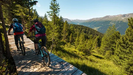 GREEN DAYS 2026 in Nauders-Reschensee
© David Karg Zwei Mountainbiker fahren auf Holzsteg in bewaldeten Berglandschaft