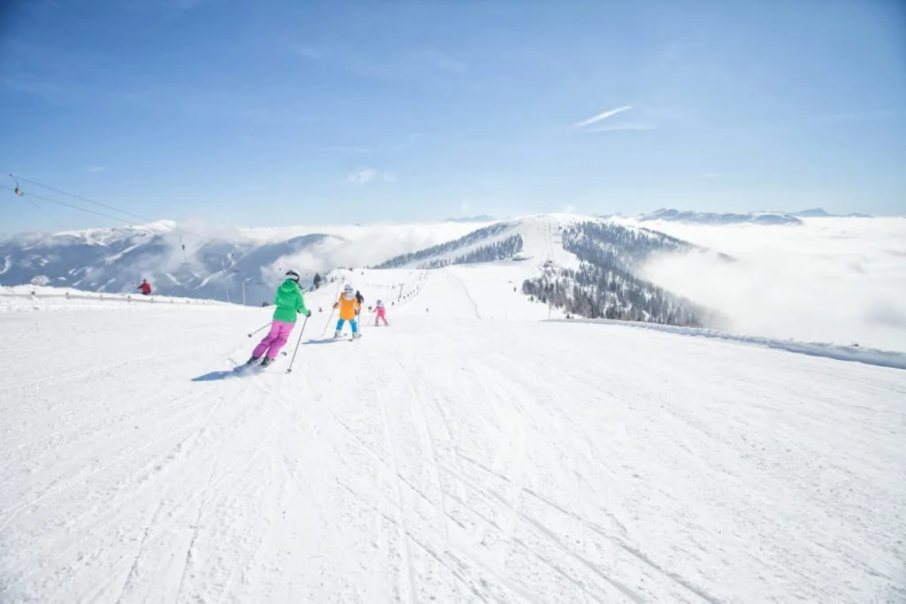 Wedelwochen – 5 Nights Skiers descend a snowy slope with mountains and clouds in the background