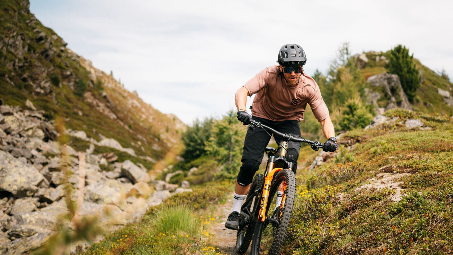 Mann fährt Mountainbike auf Bergweg mit Helm und Schutzbrille