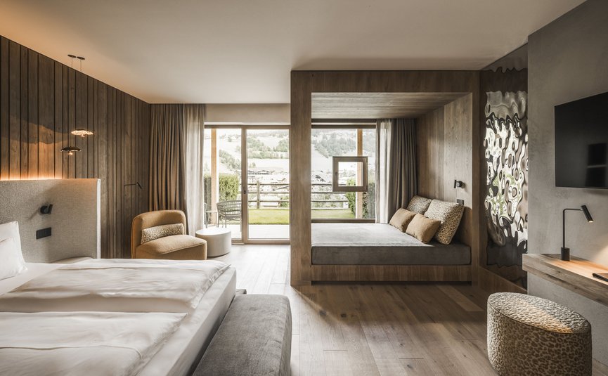 Excelsior Dolomites Life Resort ****S © Hannes Niederkofler Modern hotelkamer met bed, bank, stoelen en groot raam met uitzicht op bergen