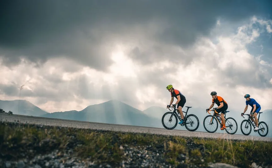 Three cyclists riding on mountain road under cloudy sky