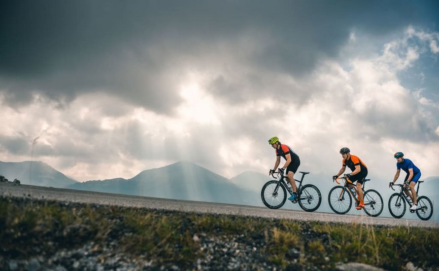Drei Radfahrer fahren auf Bergstraße bei bewölktem Himmel
