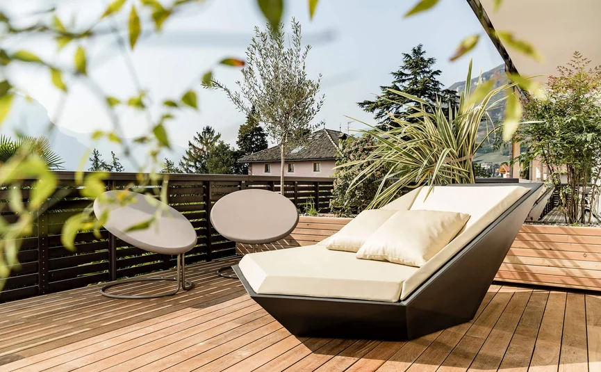Modern terrace with lounge chair, two chairs and plants in sunlight