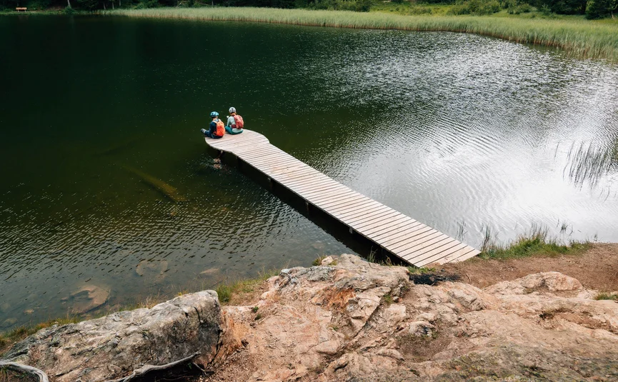 Twee fietsers zitten op een houten steiger boven een meer in de natuur