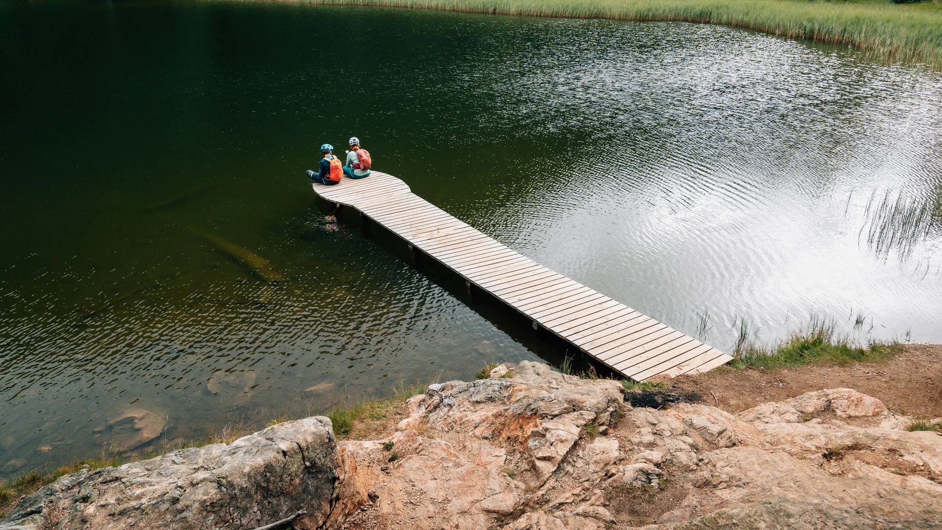 Zwei Radfahrer sitzen auf einem Steg über einem See in der Natur