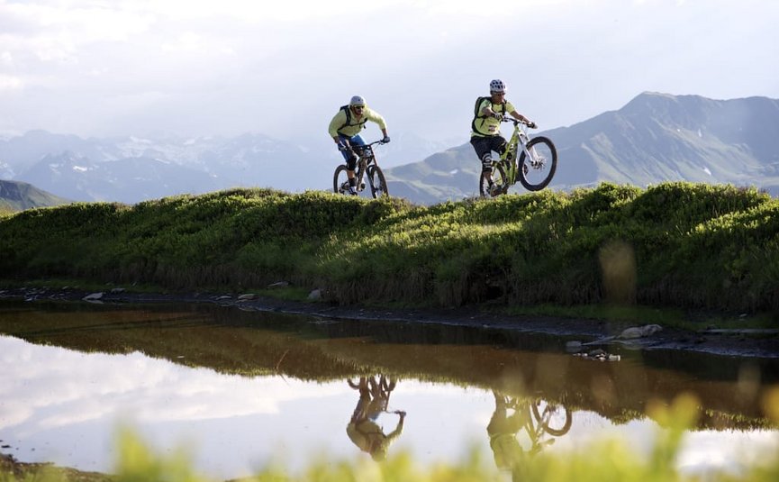 BIKE BREAK (7 Nächte) Zwei Mountainbiker fahren auf einem Hügel vor Bergkulisse mit Wasserreflexion