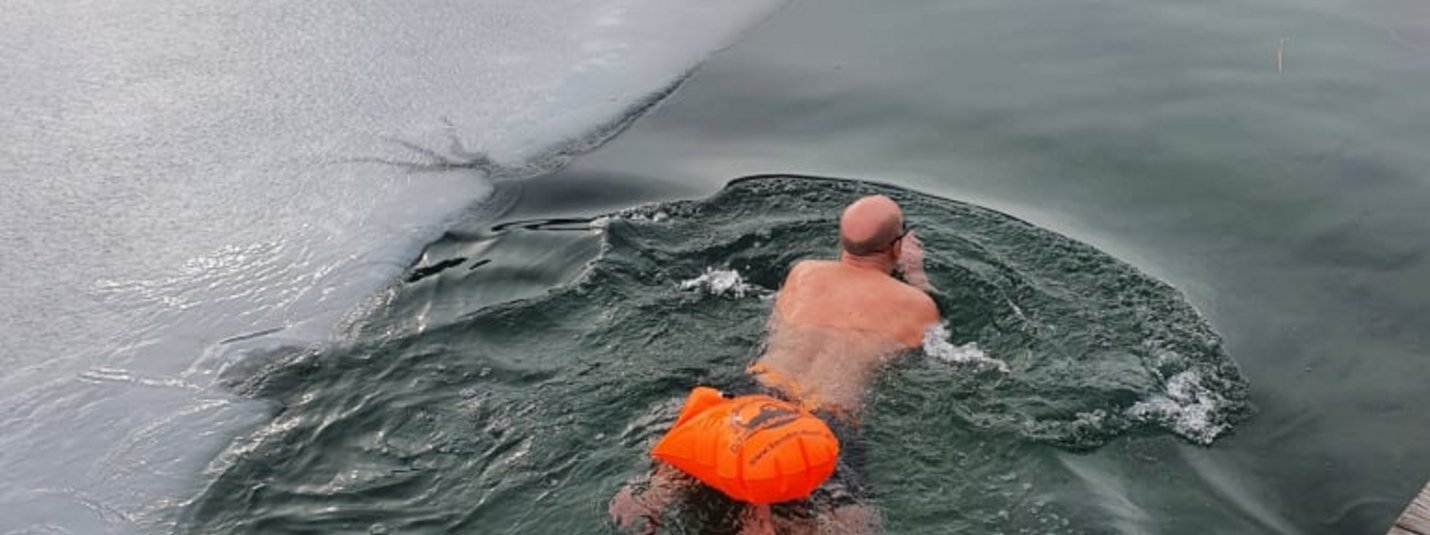Mann schwimmt in eisigem Wasser neben zugefrorenem See
