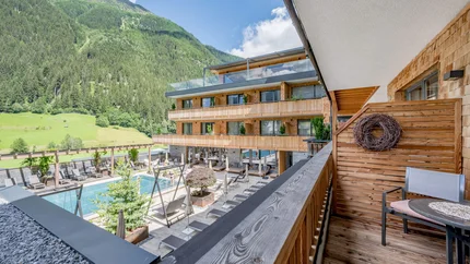 Balkon mit Blick auf Pool und Holzgebäude in den Bergen bei Sonnenschein