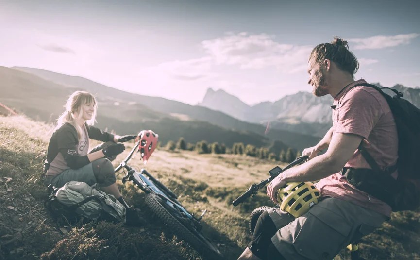 Zwei Mountainbiker machen Pause mit Bergkulisse im Hintergrund