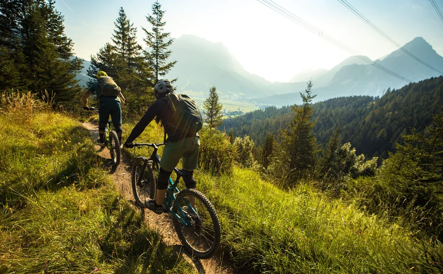 Zwei Mountainbiker fahren auf einem Bergpfad in der Sonne