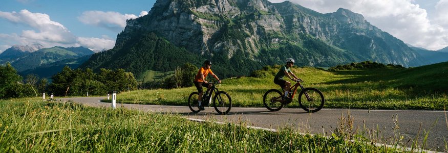 Two cyclists riding on a road with mountain scenery on a sunny day