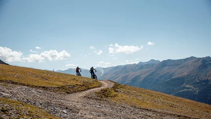 Zwei Mountainbiker fahren auf einem Bergweg bei klarem Himmel