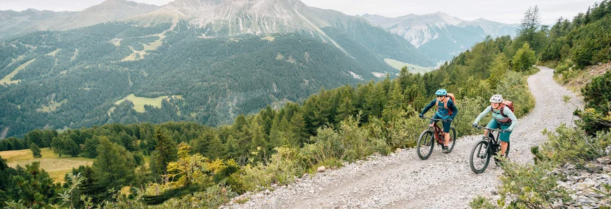 Zwei Radfahrer fahren auf einem Bergweg mit Alpen im Hintergrund