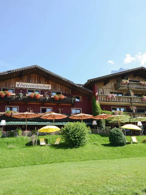 Bauernhof mit Blumen, Sonnenschirmen und Bergen unter klarem Himmel