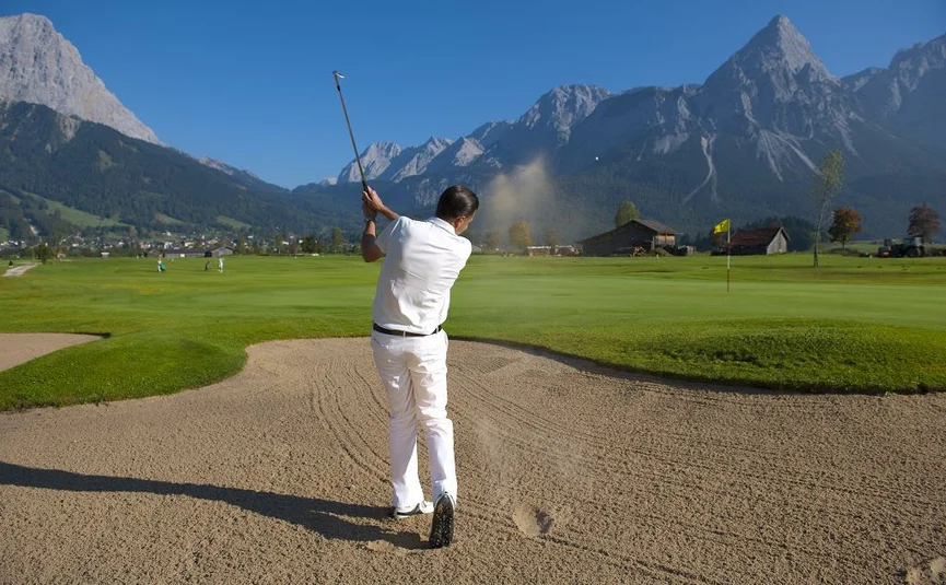 Golfer hitting ball from bunker with mountains in the background