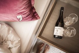 GIRLS SKI DREAM Flasche Wein und zwei Gläser auf einem Holztablett neben einem Bett mit Kissen