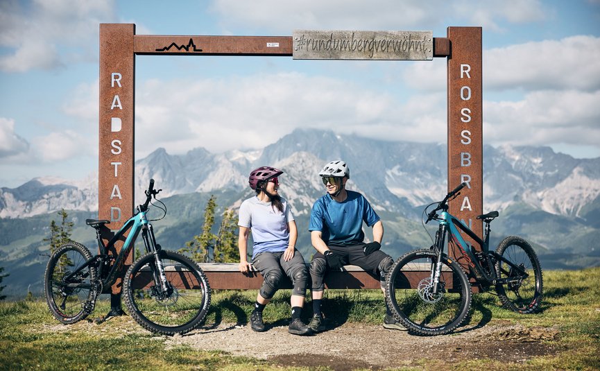 Zwei Radfahrer sitzen neben ihren Fahrrädern an einem Bergblick-Rahmen in Radstadt Rossbrand.