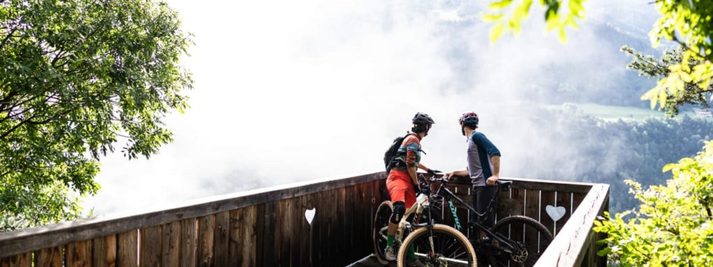 Two cyclists on a wooden viewpoint looking at a foggy valley view