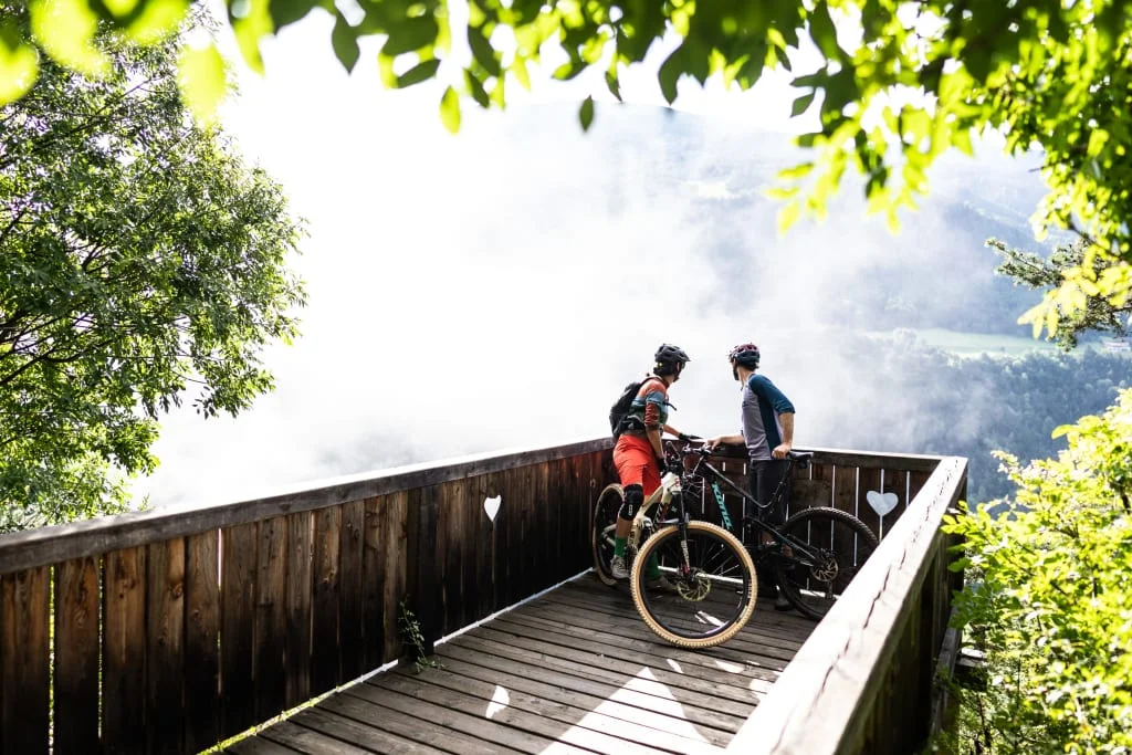 Two cyclists on a wooden viewpoint looking at a foggy valley view