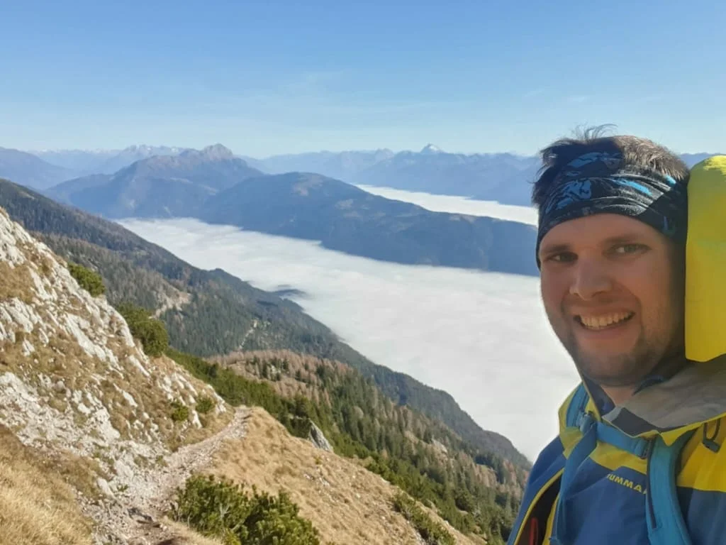 Wanderer mit Rucksack auf Bergpfad über Wolkenschicht und Bergen