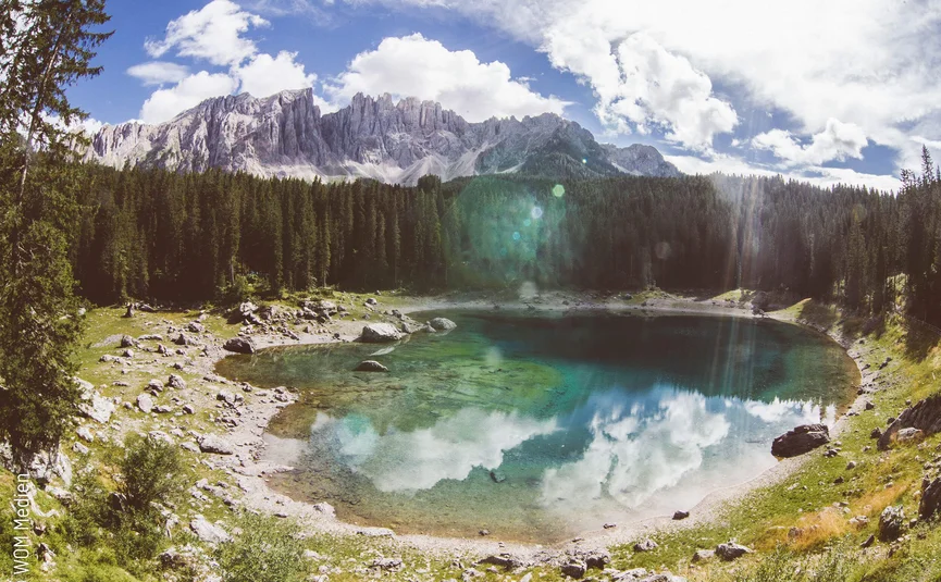 Mountain lake with clear water, surrounded by forest and mountains under blue sky