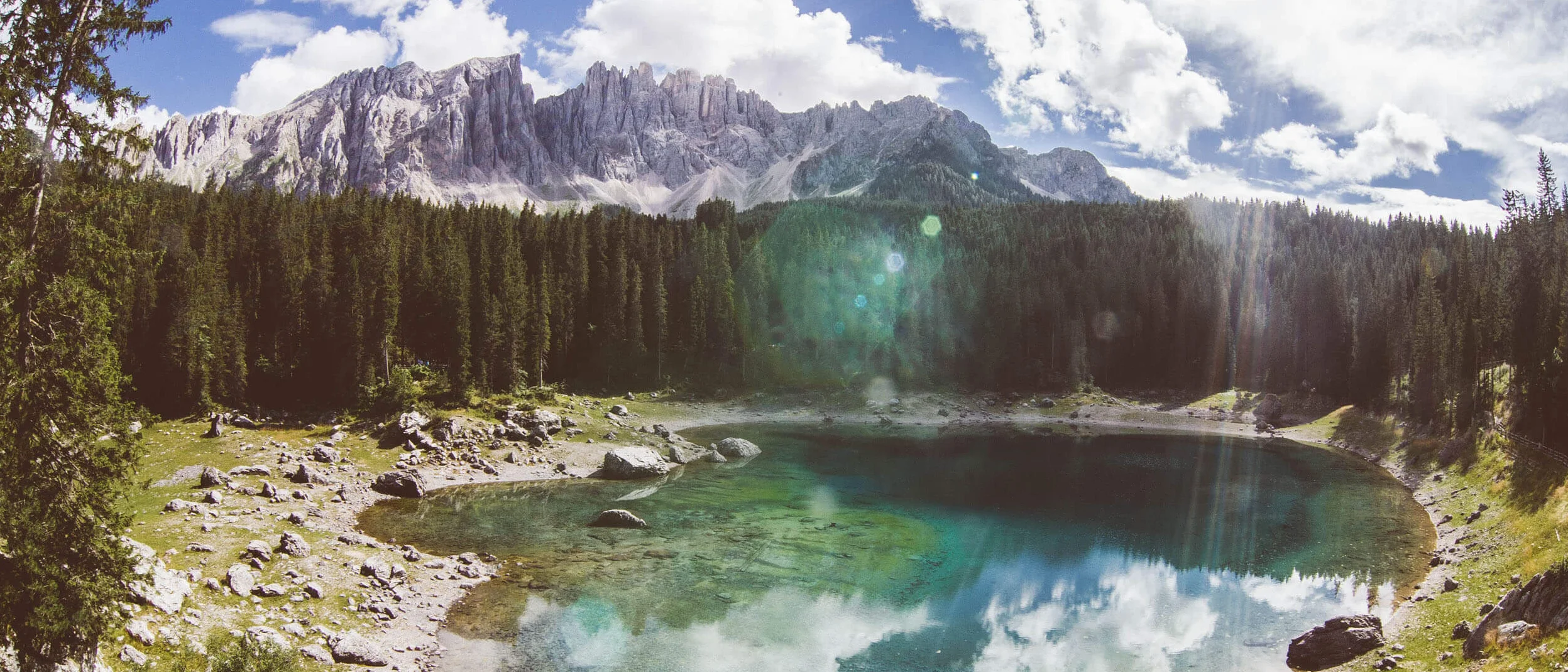 Mountain lake with clear water, surrounded by forest and mountains under blue sky