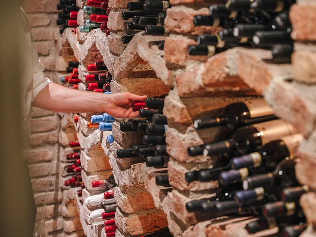 Hand nimmt Weinflasche aus einem Backstein-Weinregal
